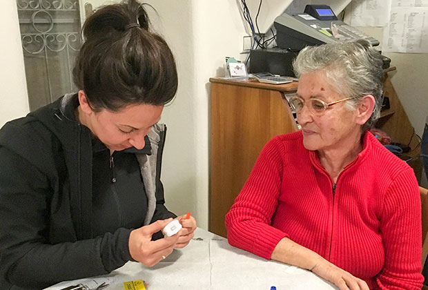 When We Band Together co-founder Zoë Pappis sits with Sophia. Lesvos local Sophia was hired by When We Band Together to sew Zoë Bands.