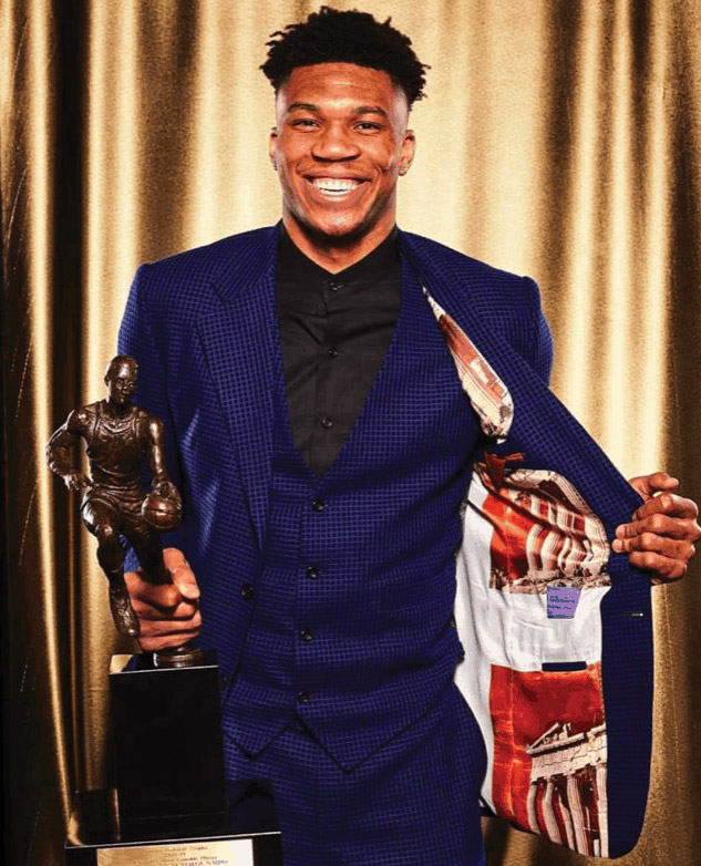 Giannis Antetokounmpo holding the MVP of the 2018-19 NBA season Award and showing his blazer with the Parthenon image