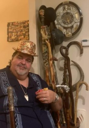 Gus Tsiavos wearing a hat he made with over 500 cigar labels using a glue gun and lacquer and holding the Al Capone cane