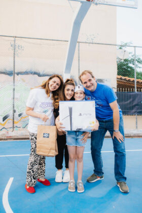 Lina Koromantzou, Novibet’s Senior Corporate Responsibility & Communications Specialist, at left, and Michael Prinztos, Greece, Country Head fpr THI, at right, present a child with a gift as part of the Roadshow’s PlayStation giveaway initiative.
