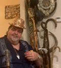 Gus Tsiavos wearing a hat he made with over 500 cigar labels using a glue gun and lacquer and holding the Al Capone cane