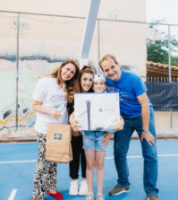 Lina Koromantzou, Novibet’s Senior Corporate Responsibility & Communications Specialist, at left, and Michael Prinztos, Greece, Country Head fpr THI, at right, present a child with a gift as part of the Roadshow’s PlayStation giveaway initiative.